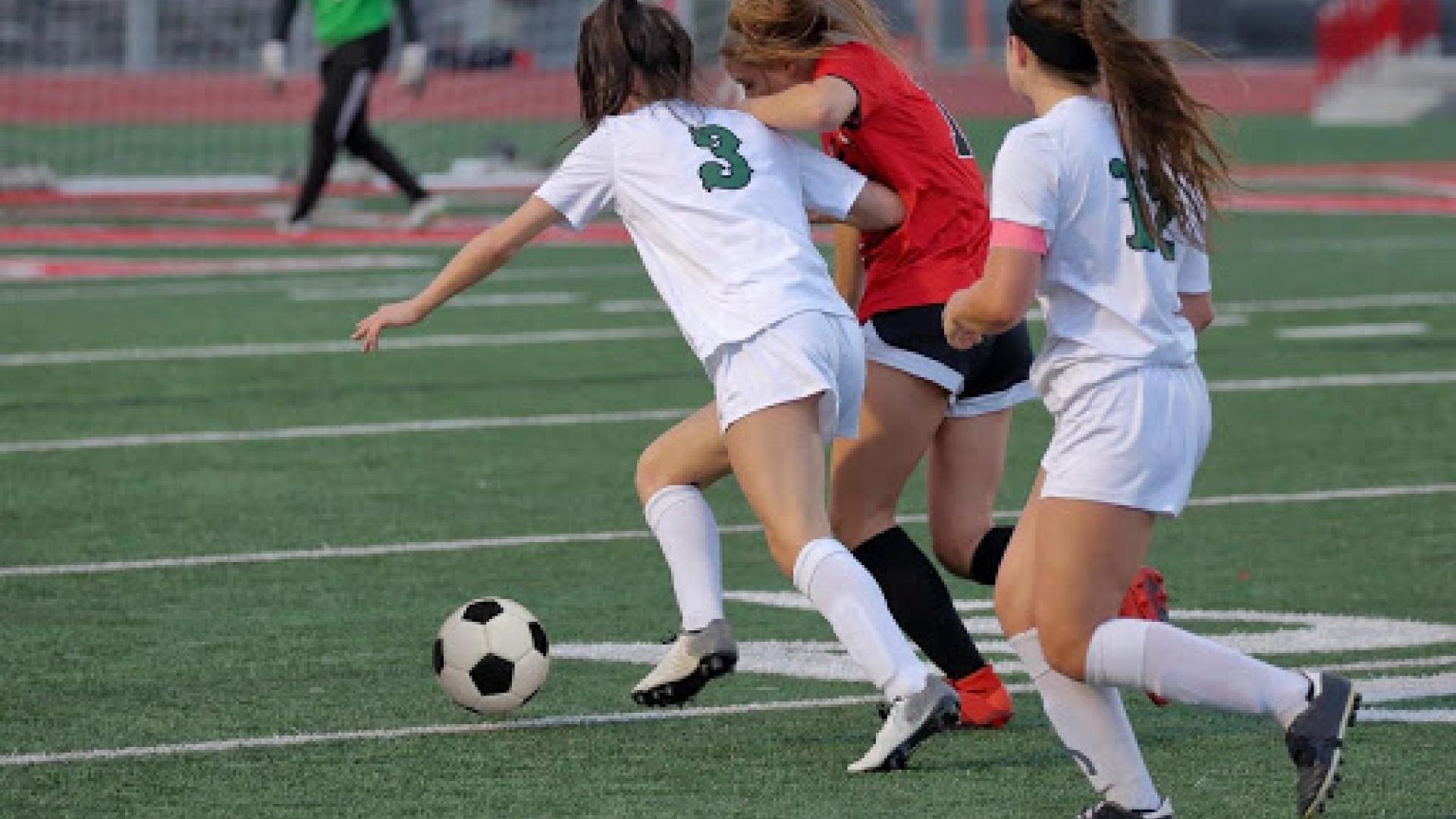 3 female soccer players chasing after the ball